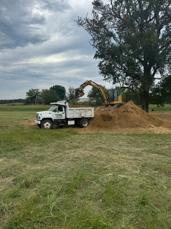 A dump truck is loading dirt into an excavator in a field.