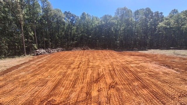 Freshly graded red dirt clearing bordered by trees under a blue sky