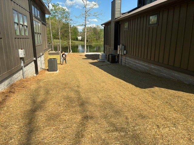 Grassy courtyard between two brown buildings, with a person and a cart in the distance under a blue sky.