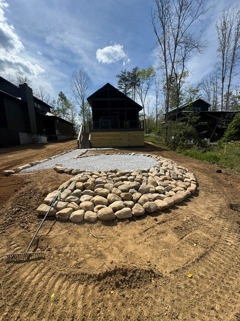 Outdoor cabin yard with a circular stone border around a white gravel pad under a blue sky
