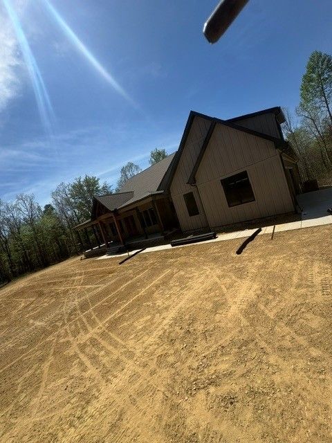 New house with beige siding and dark roof on a bare dirt lot under a bright blue sky