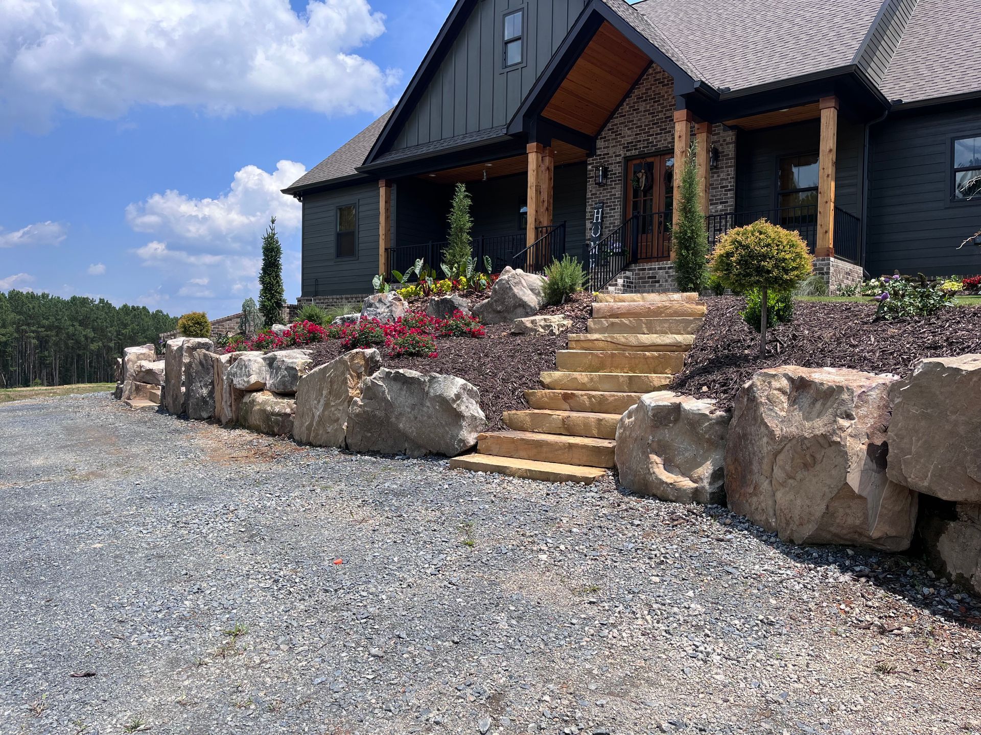 A large house with stairs leading up to it is surrounded by rocks and gravel.