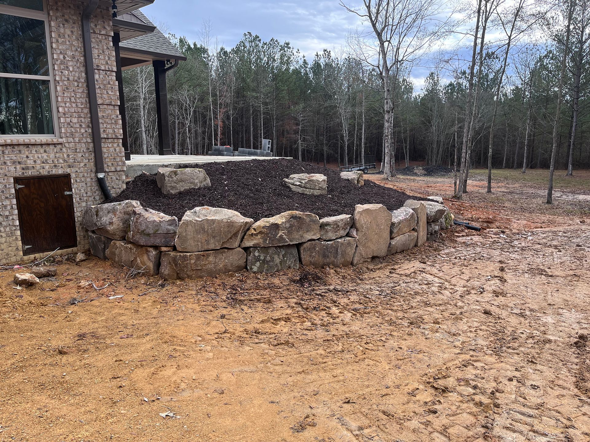 A stone wall is surrounding a house in the middle of a dirt field.