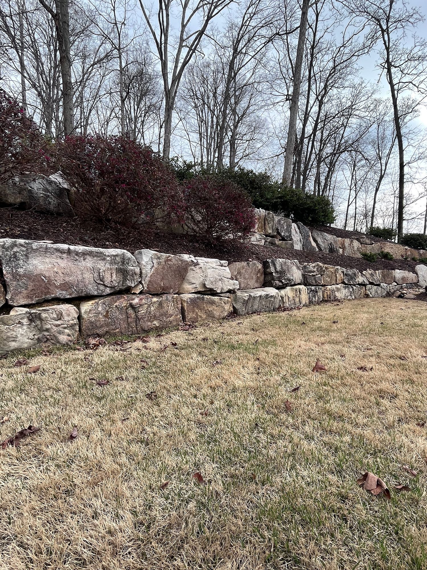 A large rock wall in the middle of a grassy field with trees in the background.