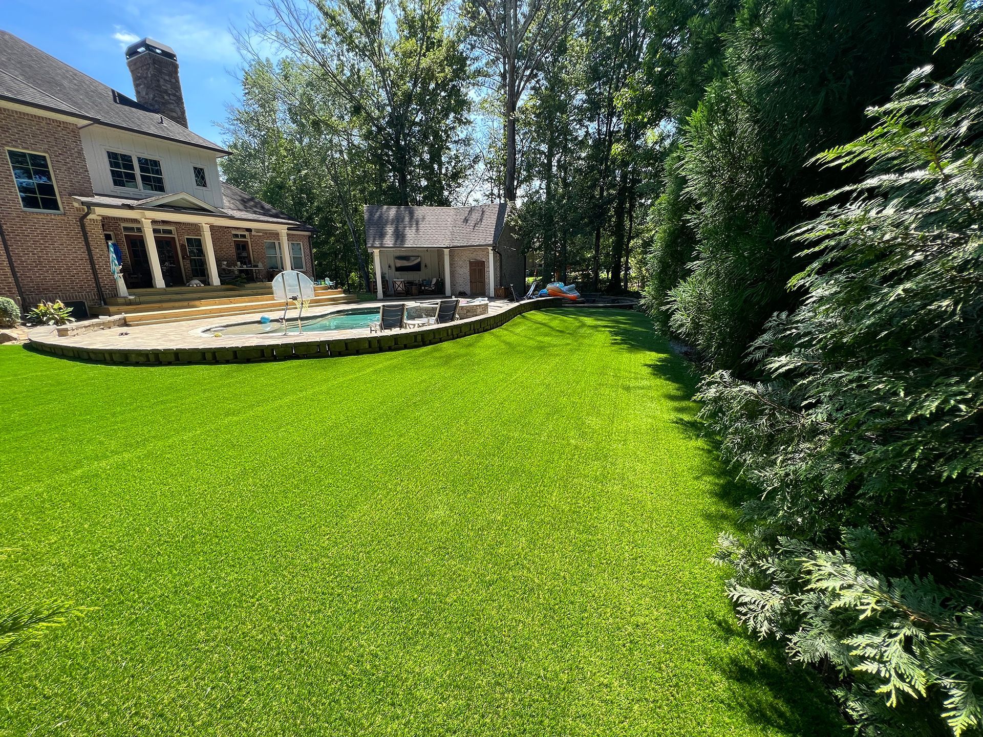 A large lush green lawn in front of a house with a pool.