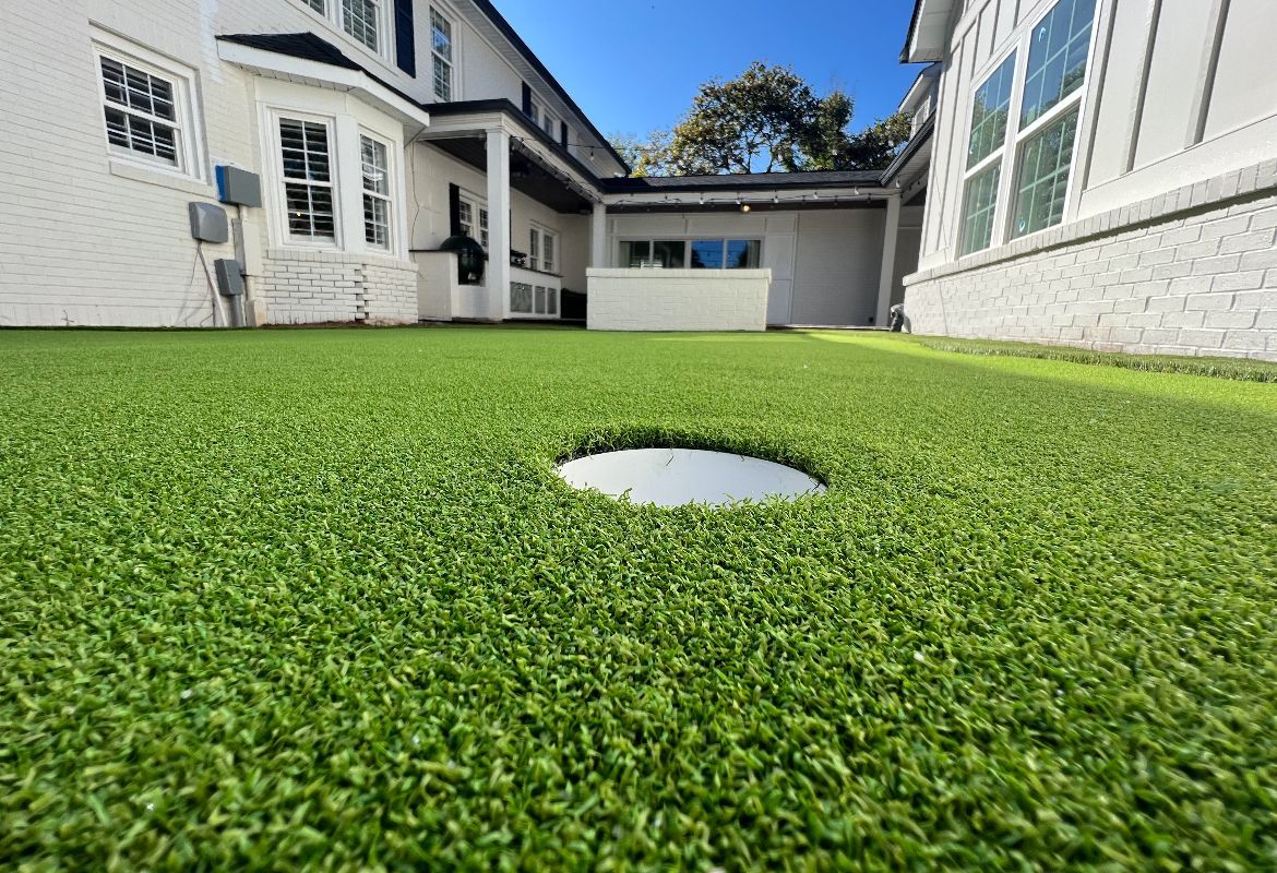 A golf course with a hole in the middle of it in front of a house.