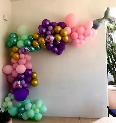 Pastel balloon garland in green, pink, purple, and gold draped along a white wall and corner