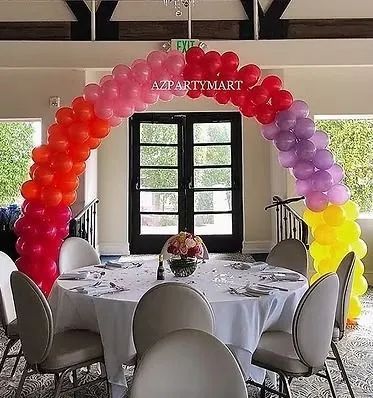 Colorful balloon arch over a round table setup in a decorated dining room with large windows