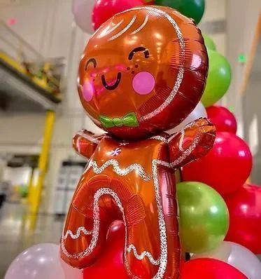 Gingerbread-man-shaped foil balloon with a smiling face and green bow tie, beside a red-and-green balloon column