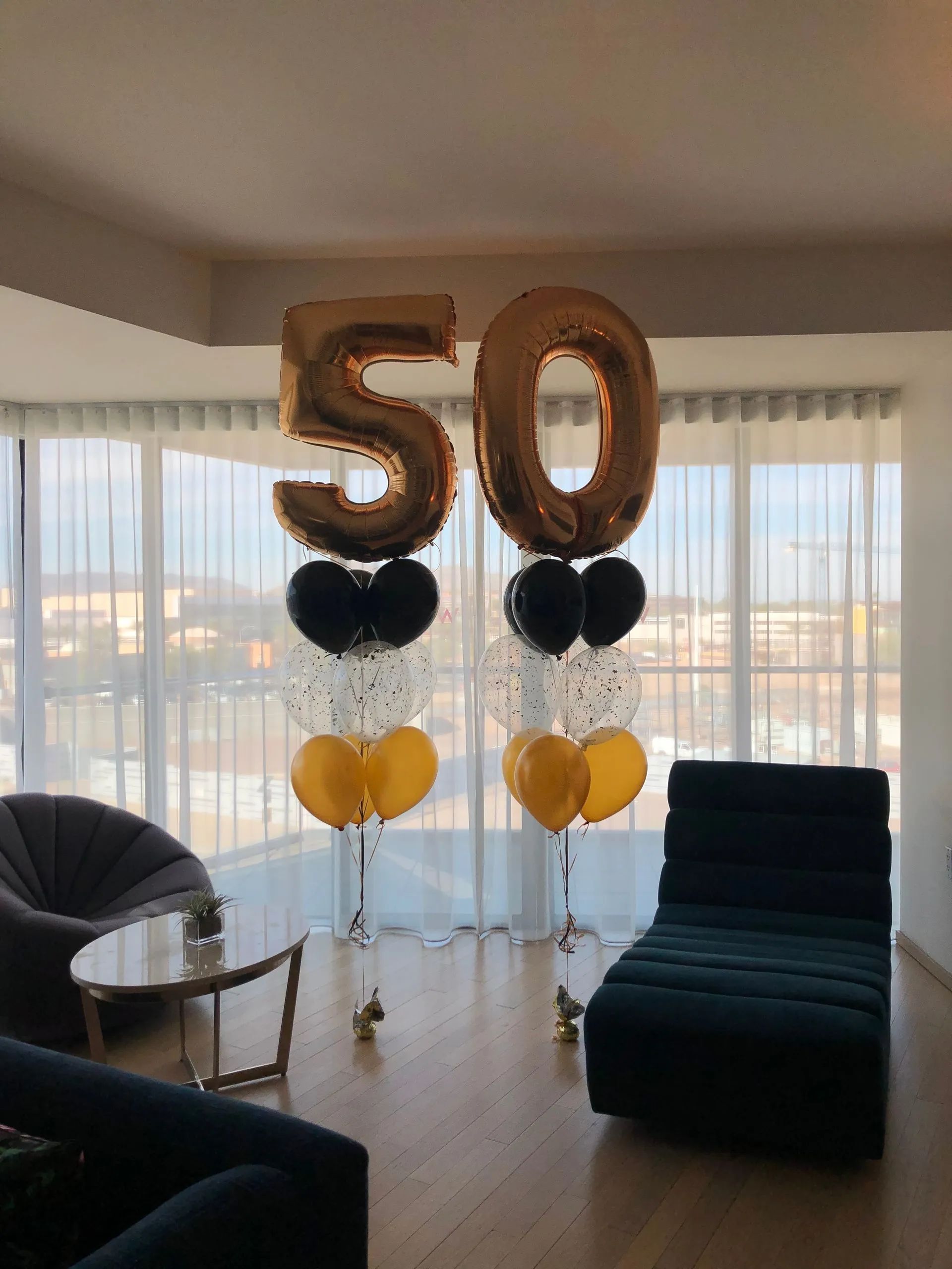 Gold “50” balloon display with black and yellow balloons by a window in a living room