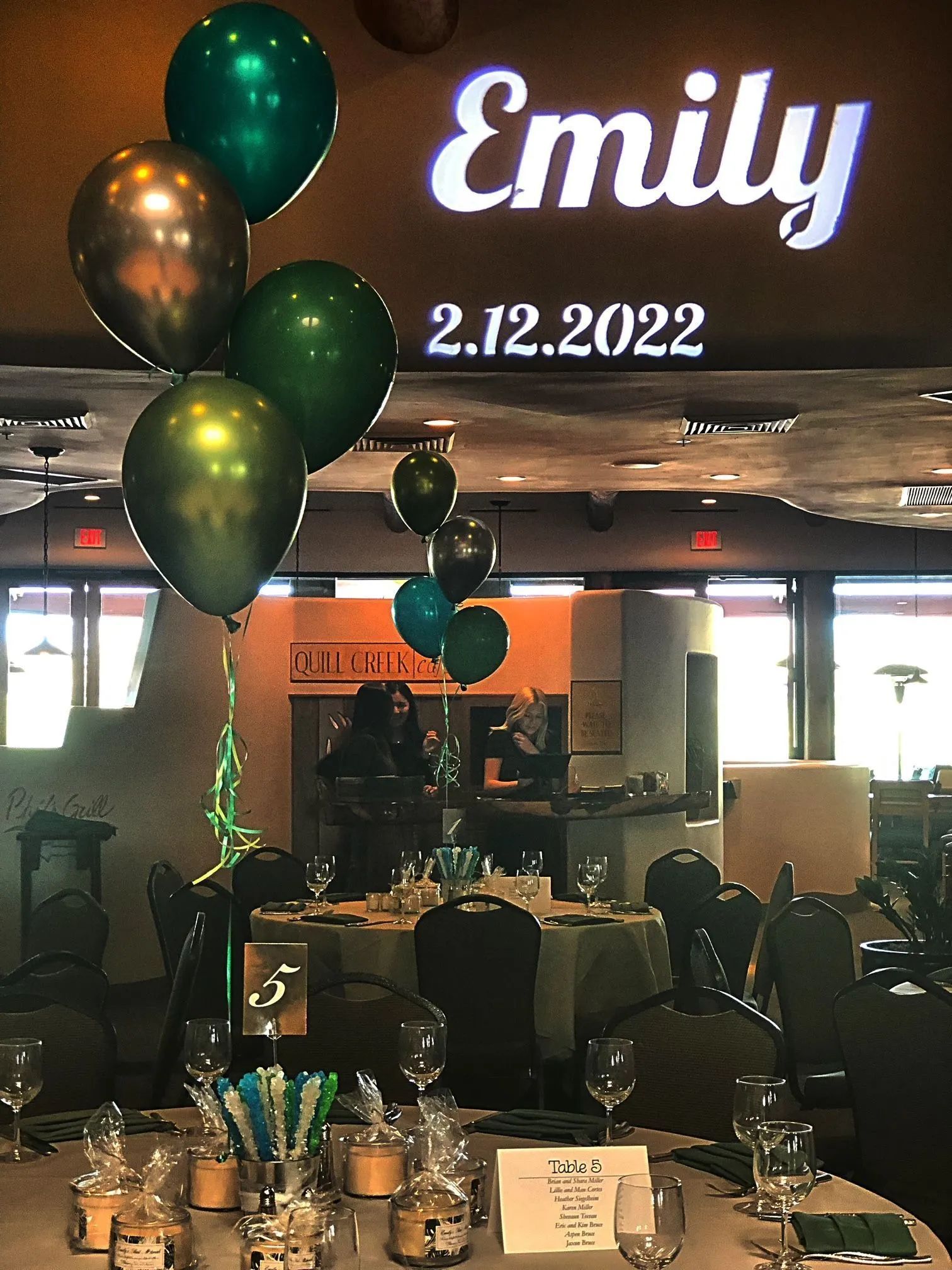Birthday celebration table with green balloons and “Emily 2.12.2022” sign in a restaurant