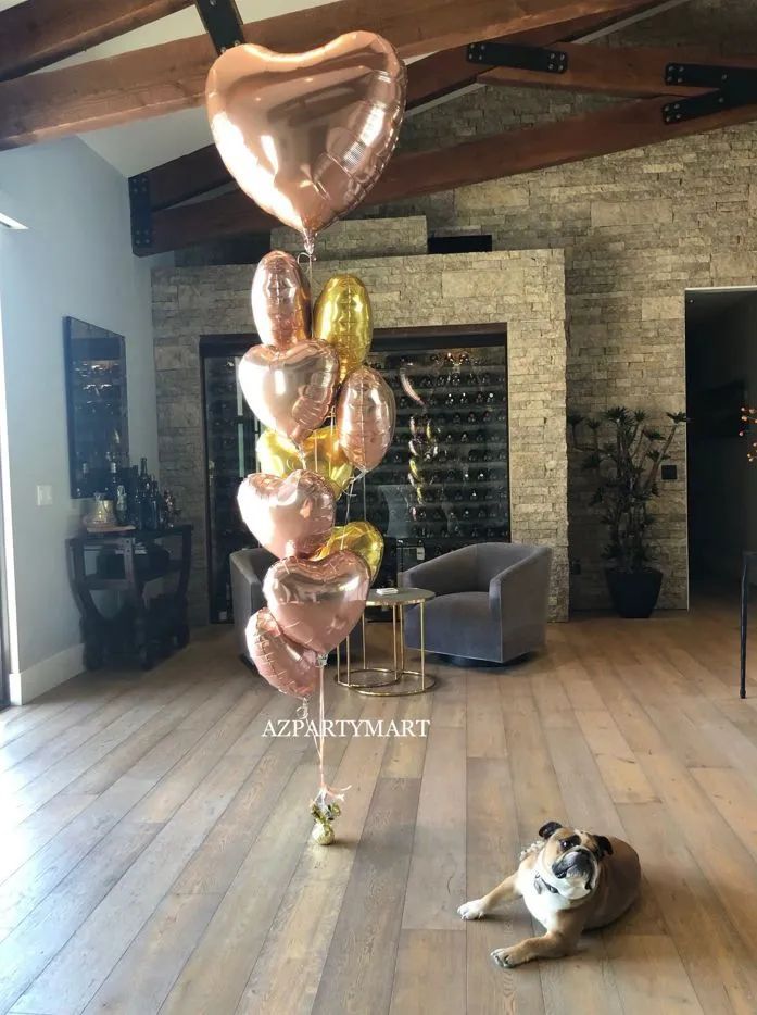 Heart-shaped rose-gold balloon tower in a living room with a dog lying on the floor.