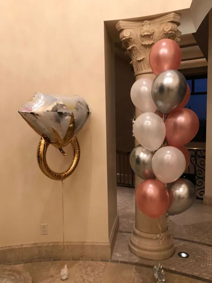 Heart-shaped silver balloon beside a column wrapped with rose gold and white balloons indoors