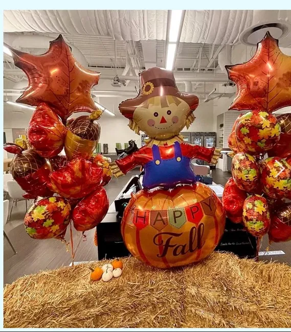 Fall display with a scarecrow, pumpkin, and orange balloon clusters in a store aisle