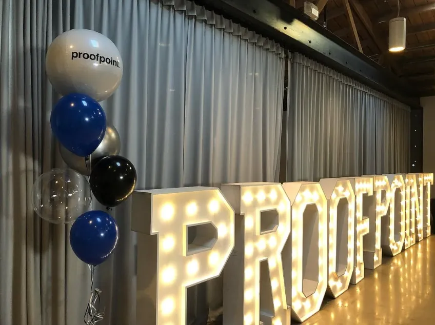 Lit marquee letters spelling “PRODUCT” beside blue, white, and black balloons in an indoor venue