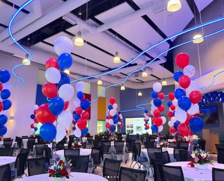 Balloon-decorated banquet hall with round tables, chairs, and hanging lights for an event