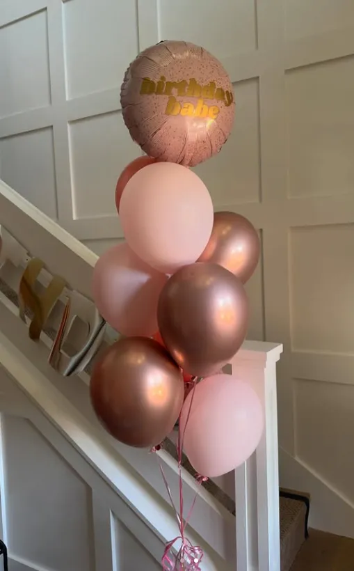 Pastel pink and rose gold balloons arranged on a staircase, topped with a gold-lettered balloon.