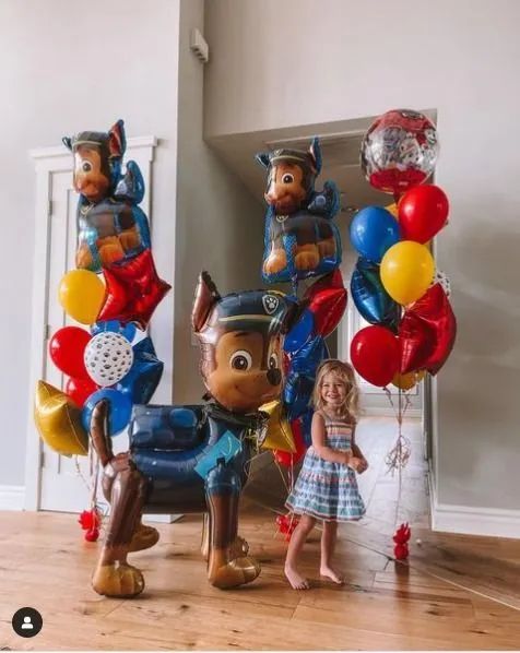 Toy horse balloons and a small doll standing on a hardwood floor, with colorful balloon bunches on both sides