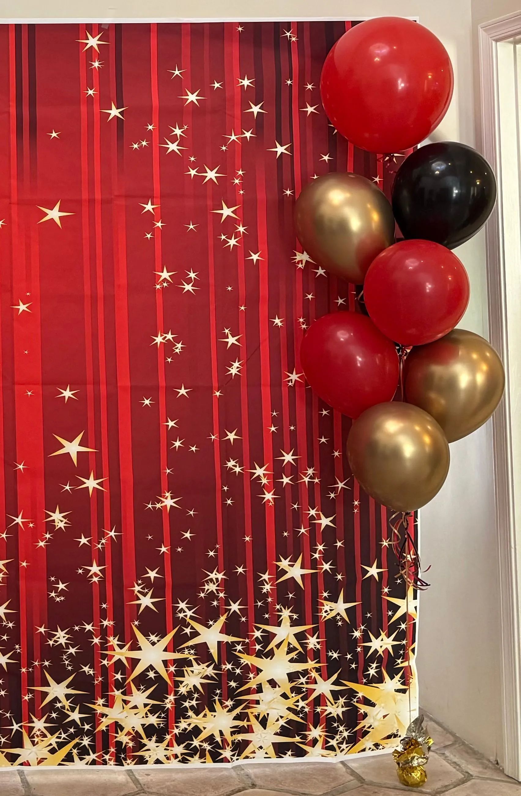 Red and gold balloon arch beside a red starry backdrop with gold confetti at the base