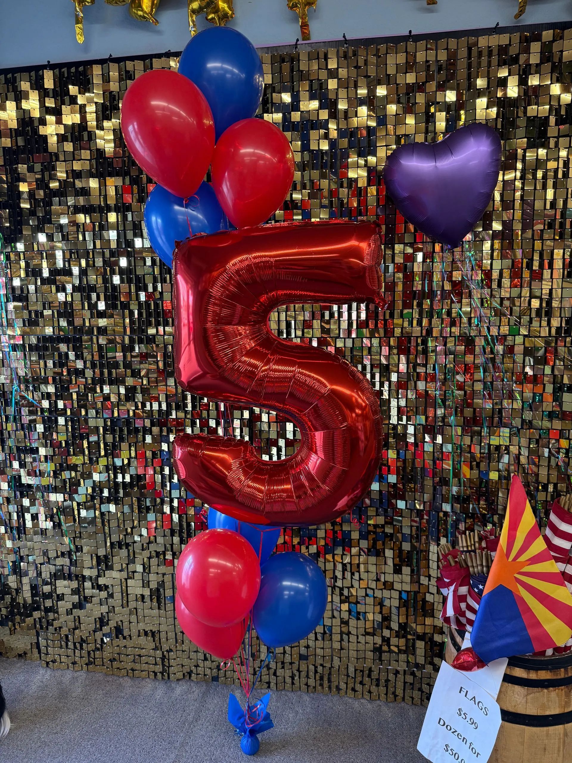 Large red number 5 balloon surrounded by red, blue, and purple balloons against a gold sequin backdrop.