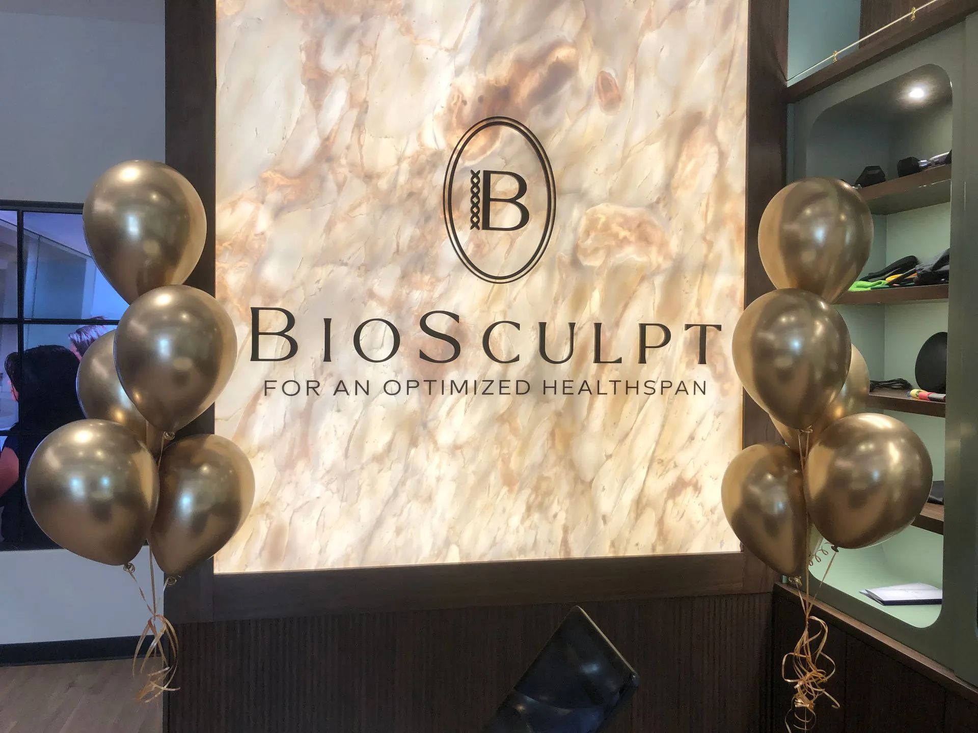 Biosculpt reception sign with gold and black balloons in a modern spa lobby