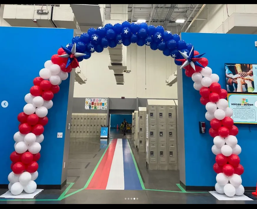 Red, white, and blue balloon arch over a hallway entrance with matching floor stripes