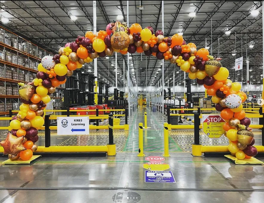 Balloon arch at warehouse entrance, with yellow safety gates and stop signs in the aisle