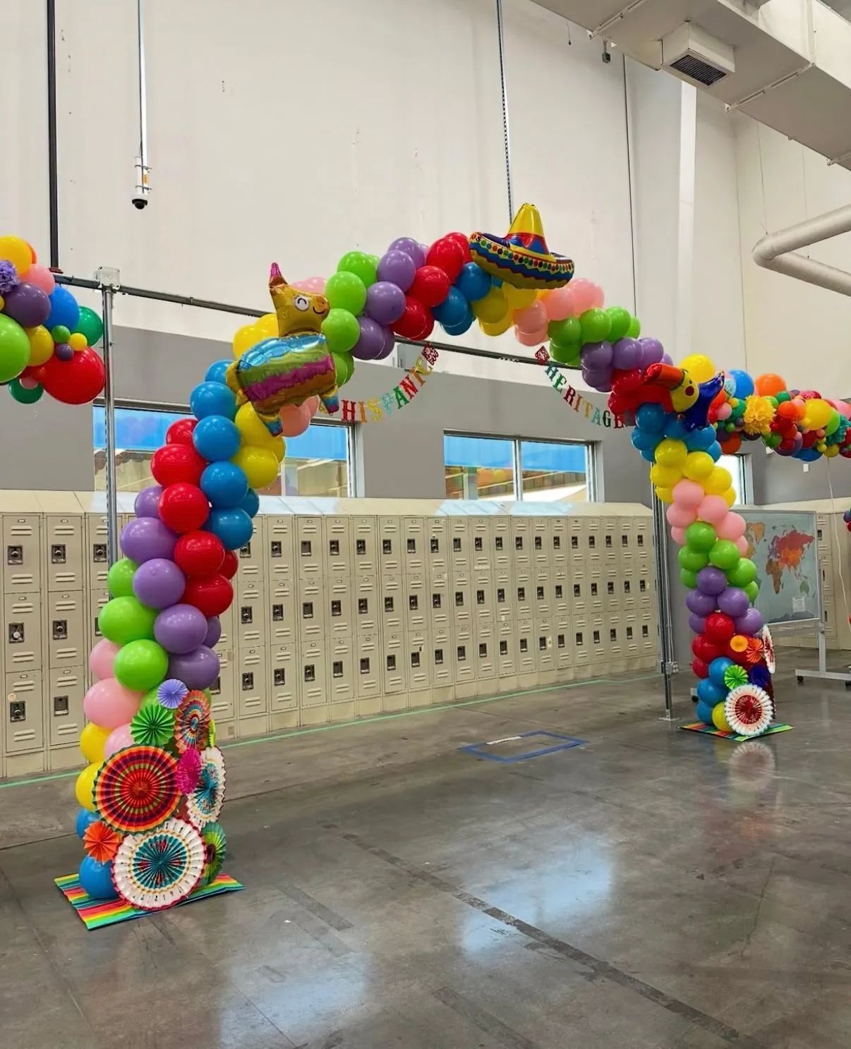 Colorful balloon archways decorate a school hallway with lockers and reflective floors