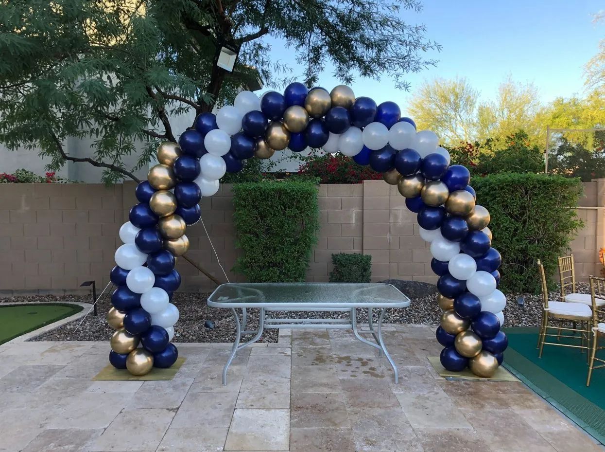 Blue and gold balloon arch over a metal table in a patio courtyard