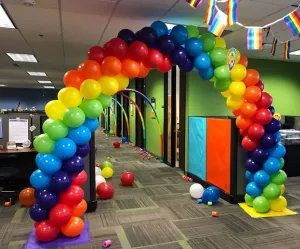 Rainbow balloon arch in an office hallway with scattered balloons and colorful decor