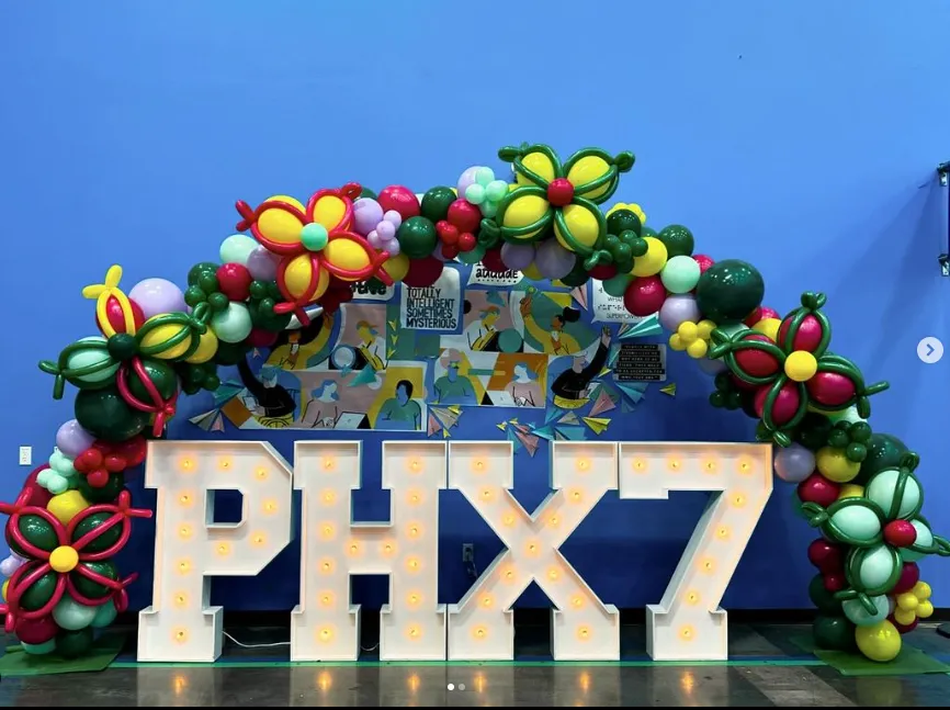 PHX7 sign under a colorful balloon arch against a blue backdrop