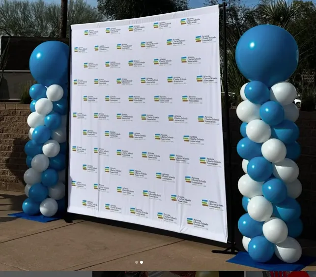 White event backdrop between two blue-and-white balloon pillars outdoors