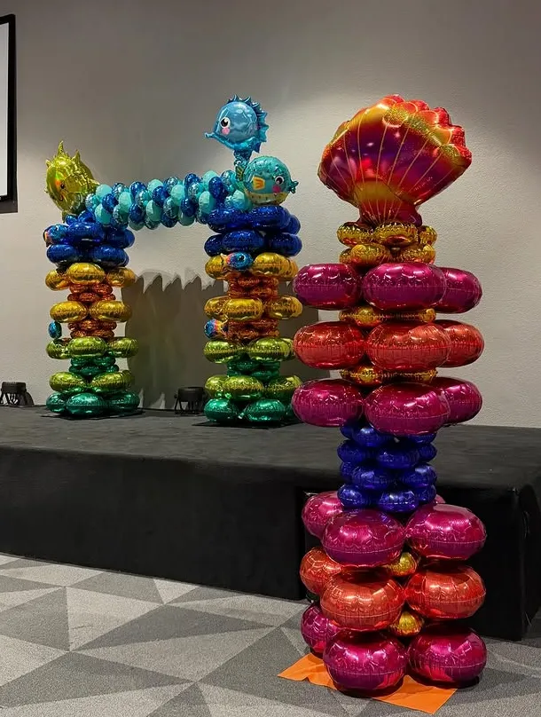Colorful stacked-sculpture arches and columns on a black platform in a gallery, with a patterned floor.