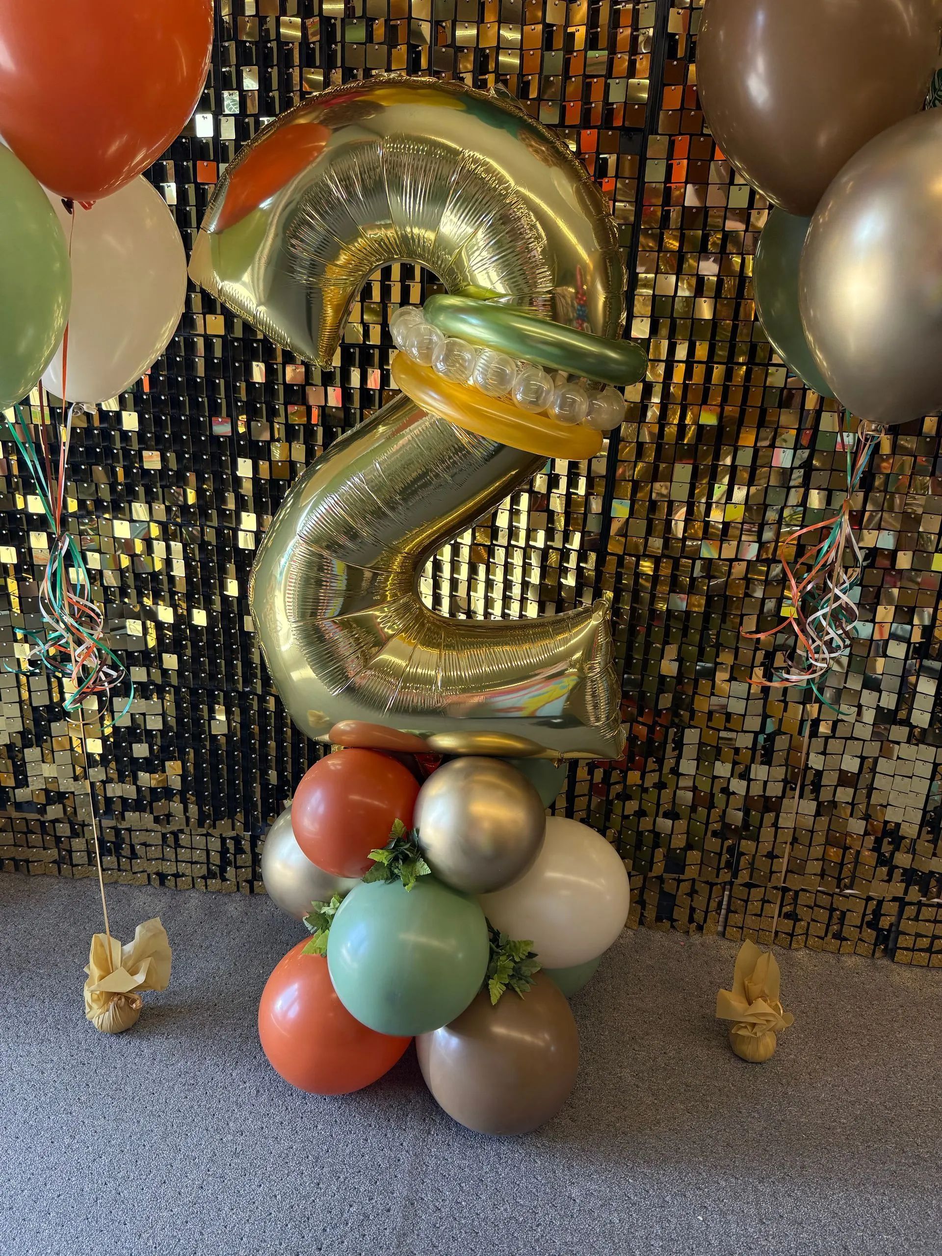 Gold balloon number 2 centerpiece with colorful balloon clusters against a glittery backdrop