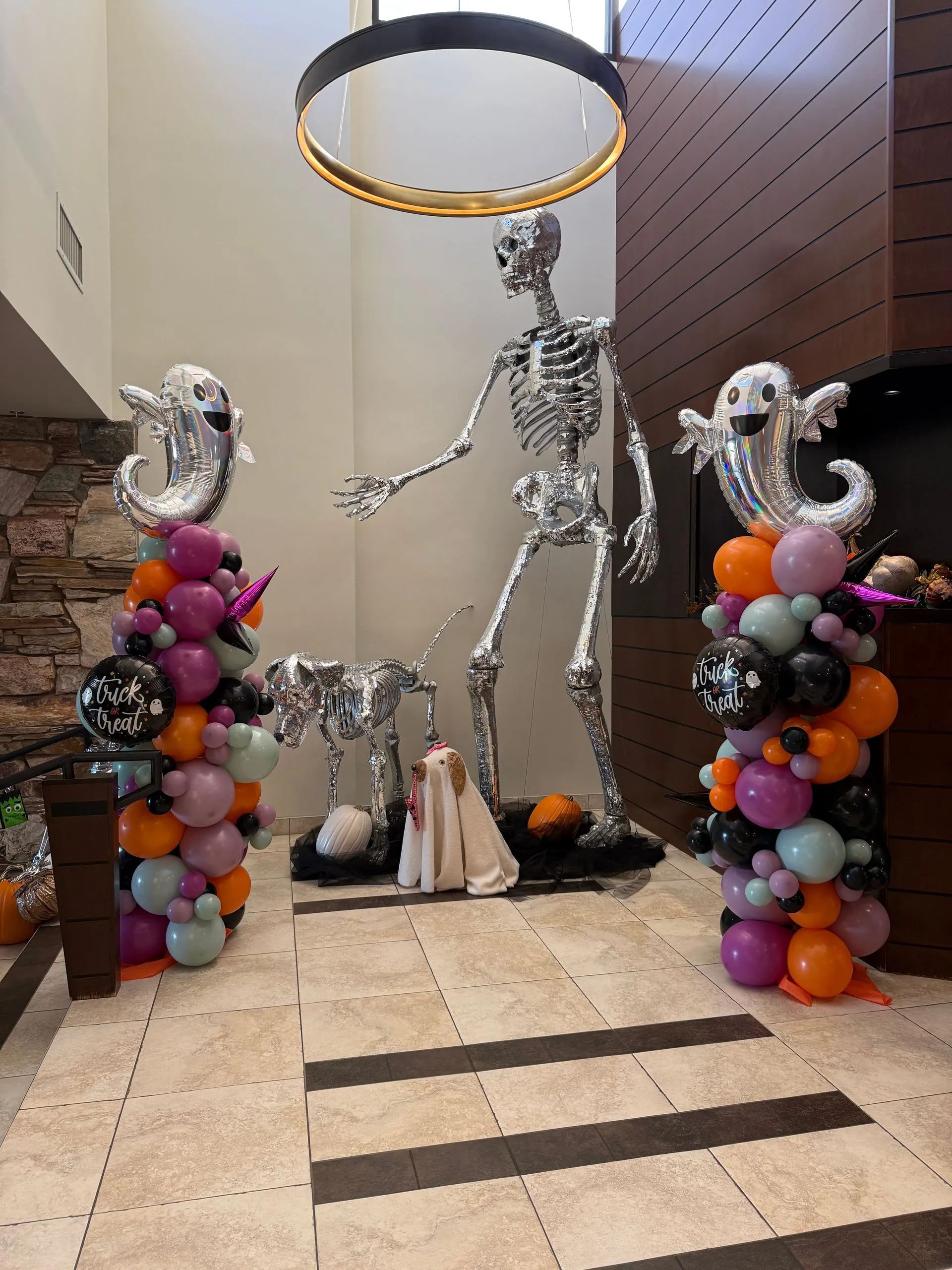 Skeleton Halloween decor with balloon columns and pumpkins in a tiled entryway