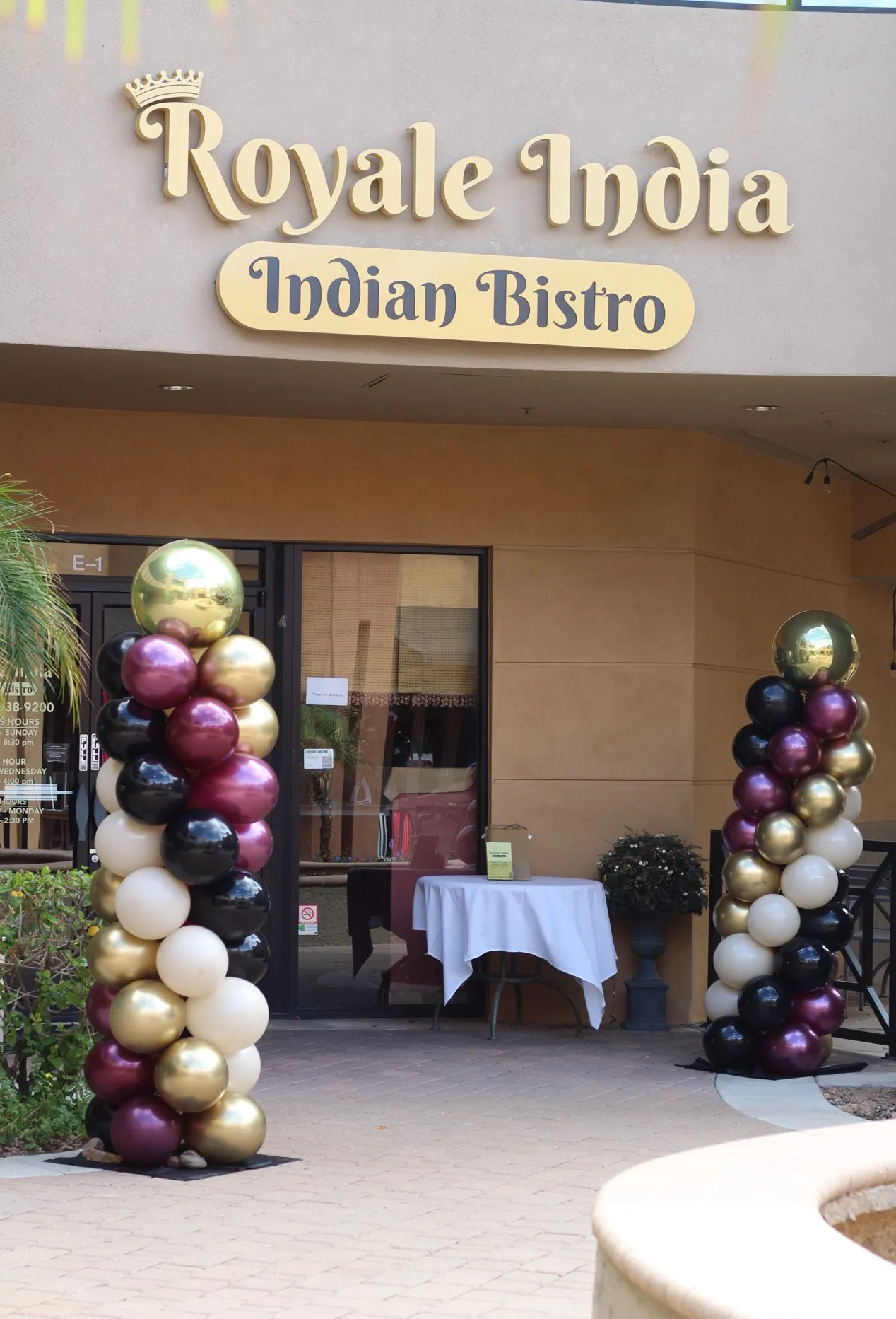 Entrance to Royale India Indian Bistro with balloon columns and a small table under the sign