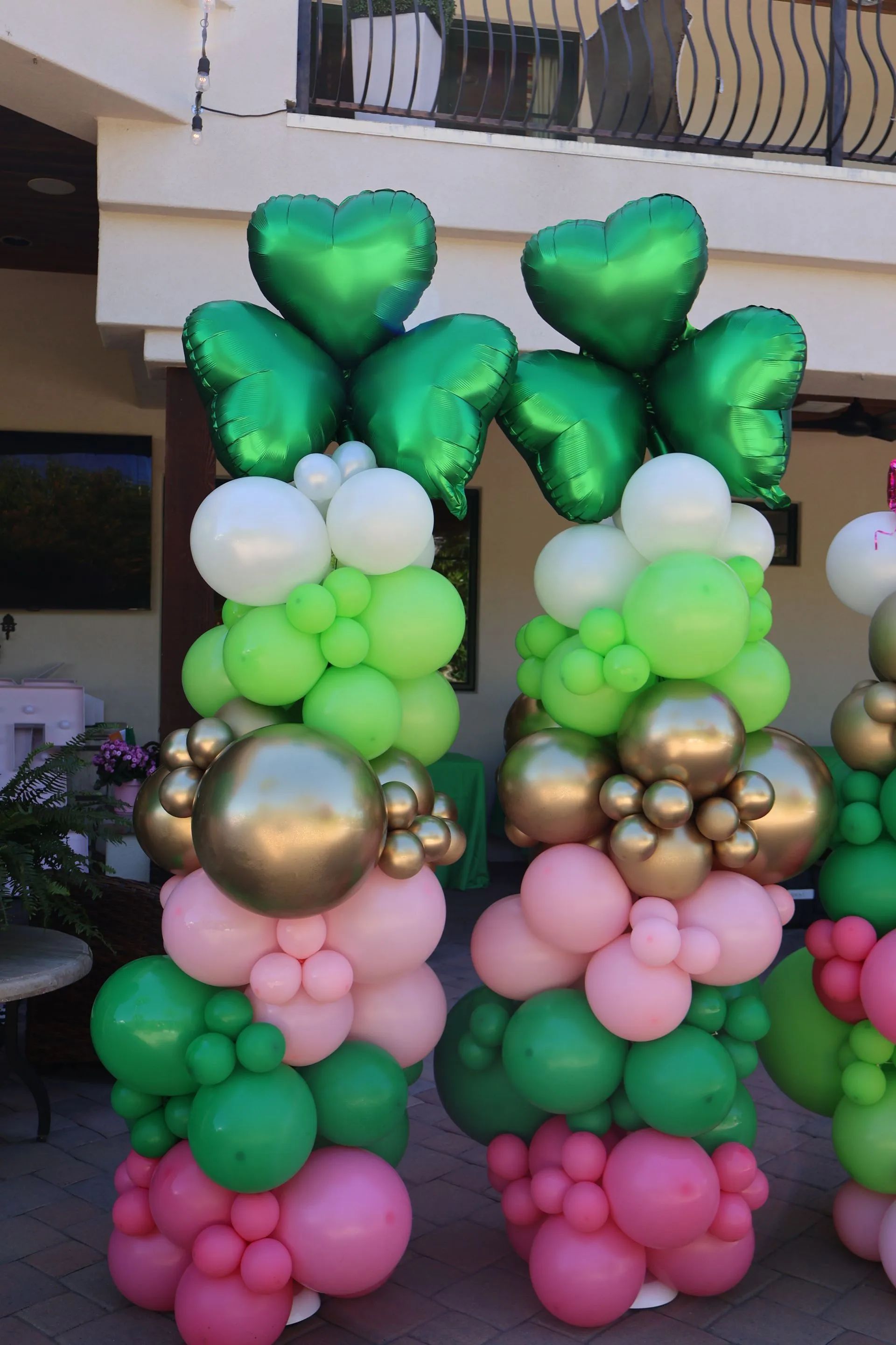 Decorative balloon columns in green, white, gold, and pink outside a building