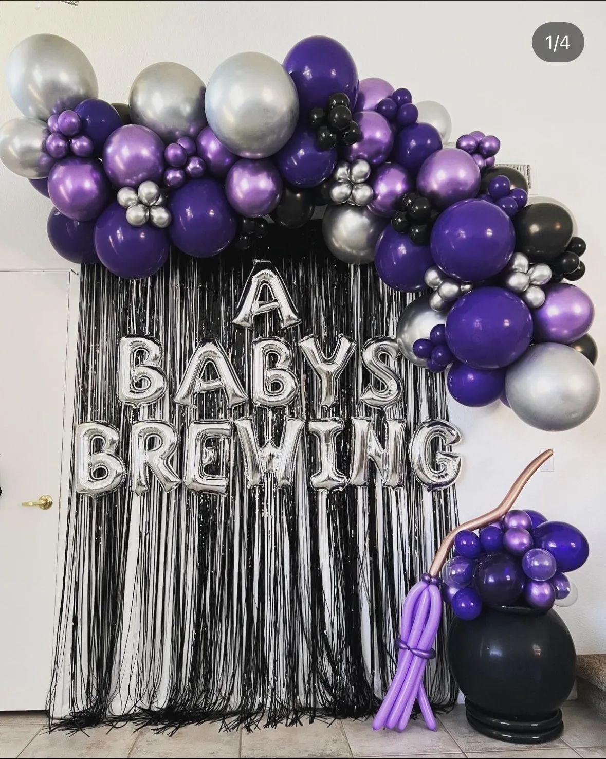 Black and purple balloon arch with silver accents over “A Baby is Brewing” backdrop and matching table decor