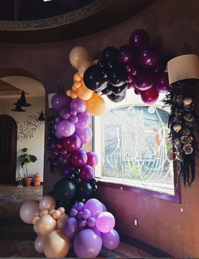 Purple, black, gold, and white balloon garland around a bright window in a decorated indoor room