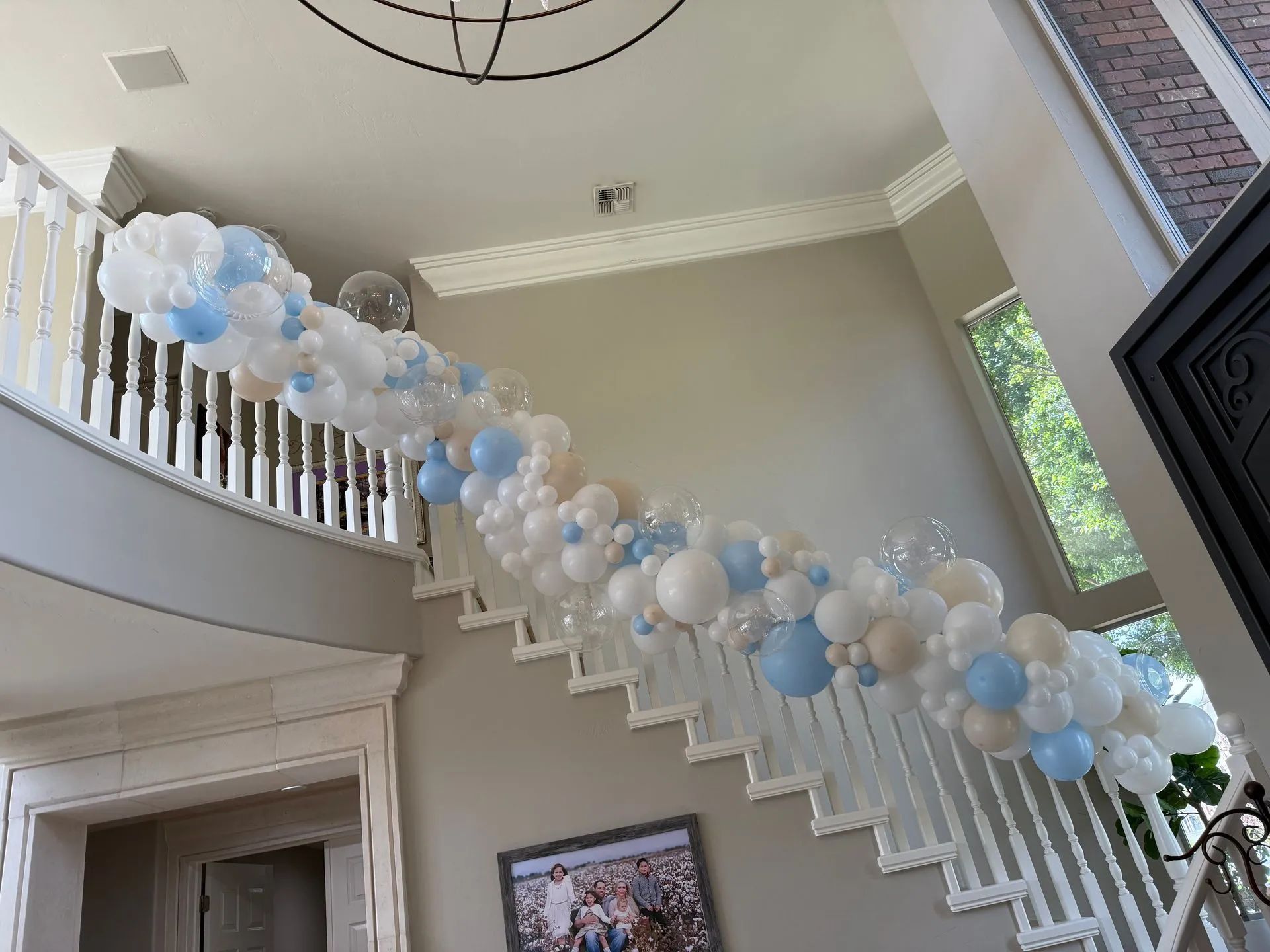 Blue and white balloon garland draped along a staircase in a bright foyer