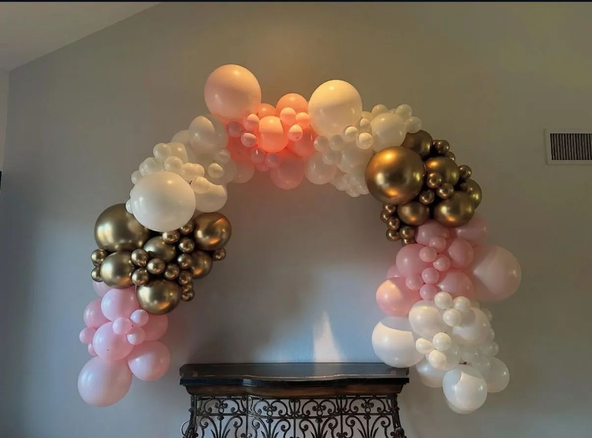 Pastel and gold balloon arch above a console table in a gray room