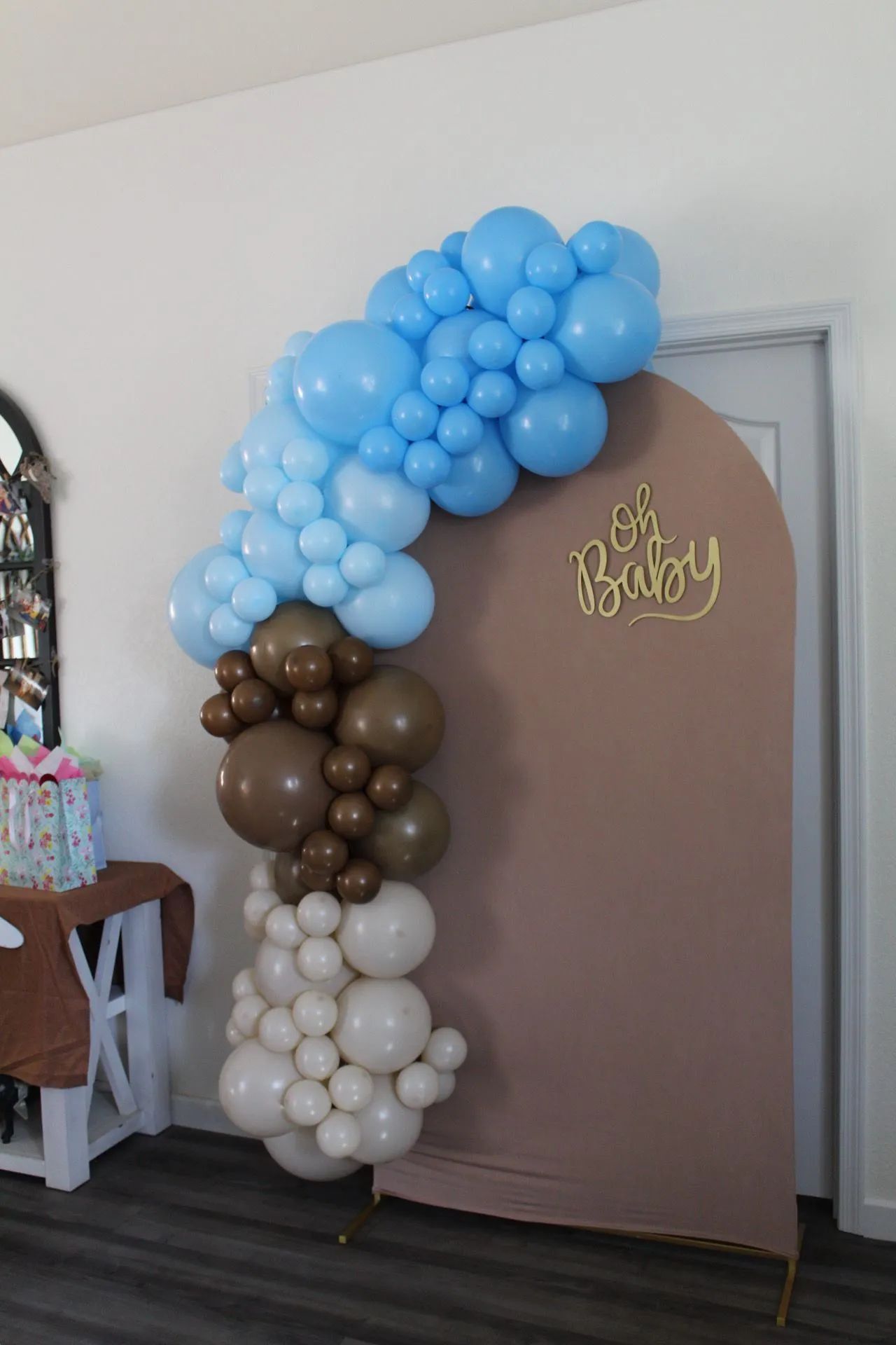 Balloon arch in blue, brown, and white beside a brown backdrop with “Oh Baby” sign