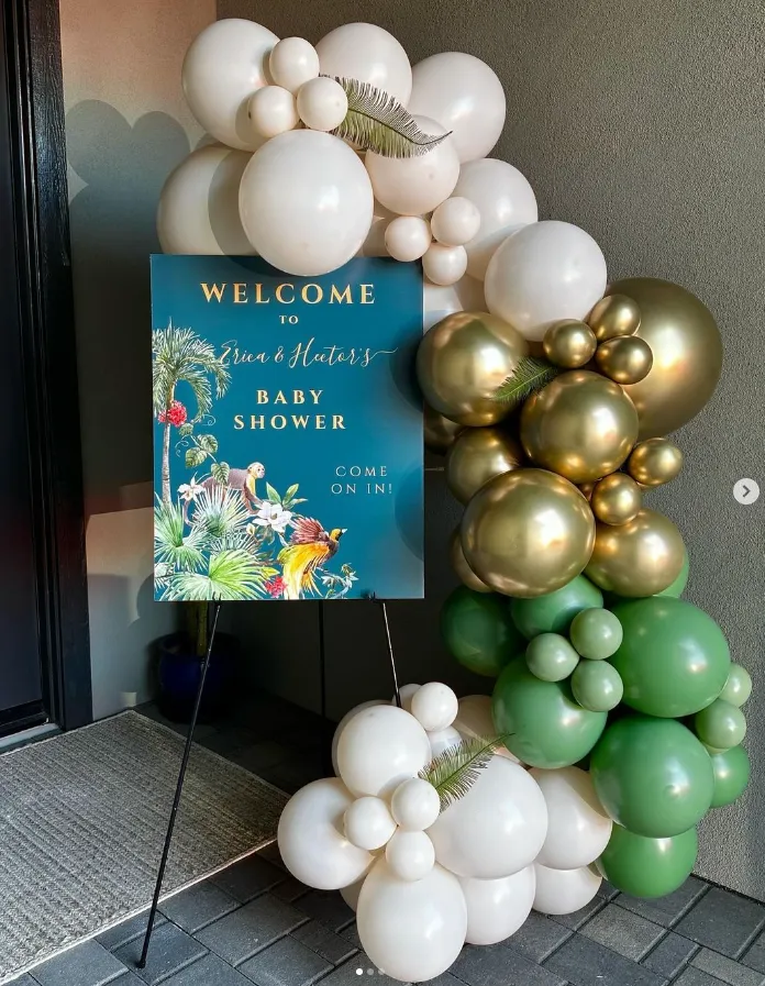 Baby shower welcome sign with gold, green, and white balloon arch in an entryway