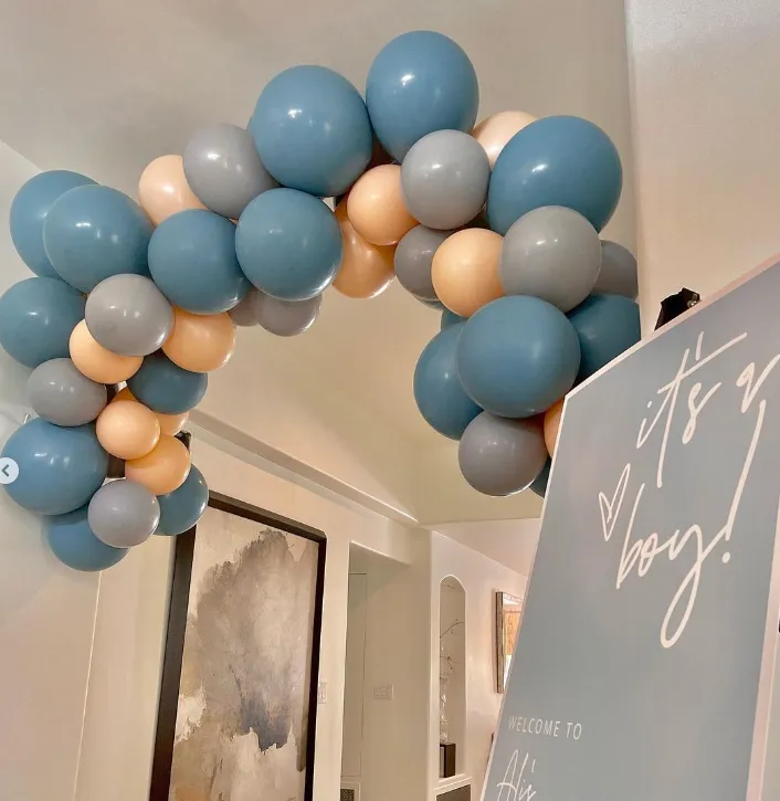 Blue, white, and beige balloon arch over a sign reading “It’s a boy!” in a home entryway