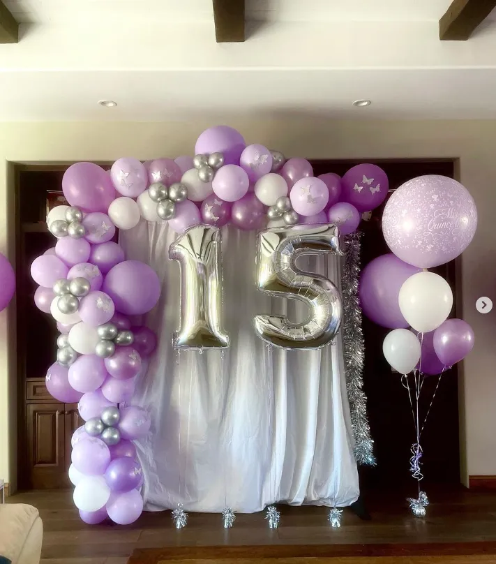Purple and silver balloon arch with large gold “15” numbers over a white backdrop for a birthday celebration