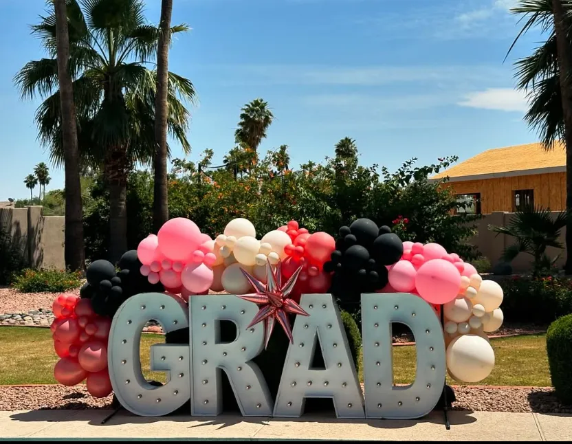 GRAD balloon display with pink, black, and white balloons in a sunny outdoor yard