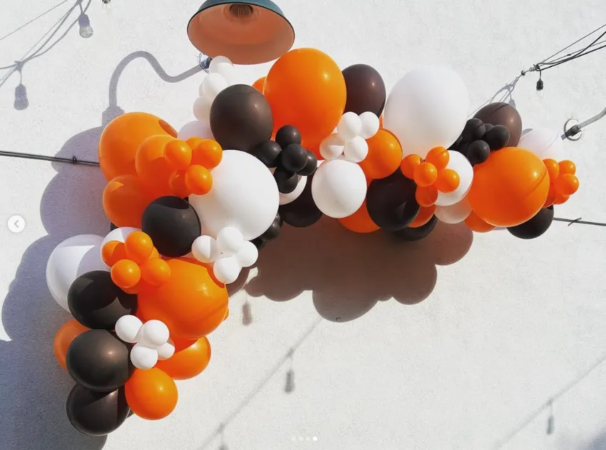 Black, orange, and white balloon arch on a wall with string lights