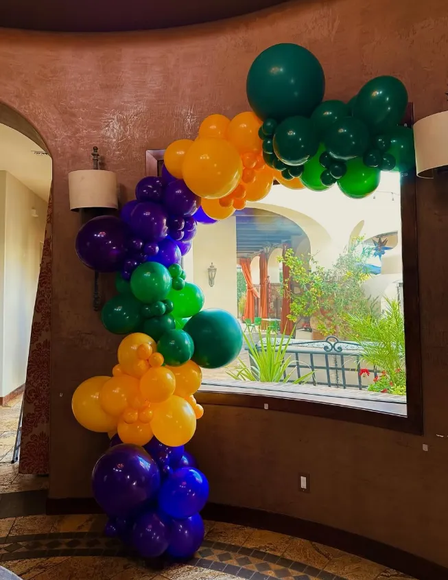 Colorful balloon arch in purple, green, yellow, and teal frames a window in a lobby.