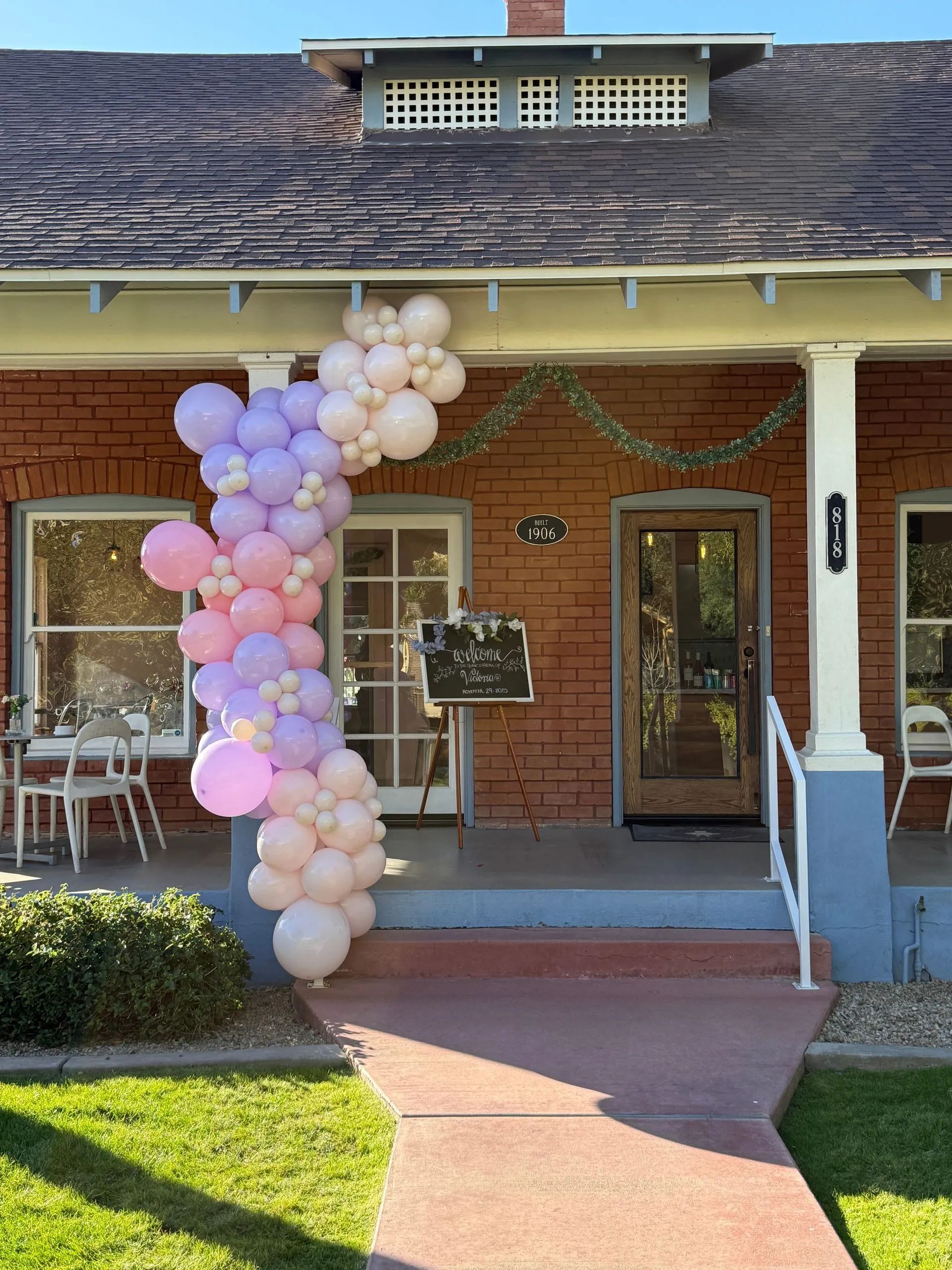 Pink and white balloon arch decorating a brick house porch with front door and walkway