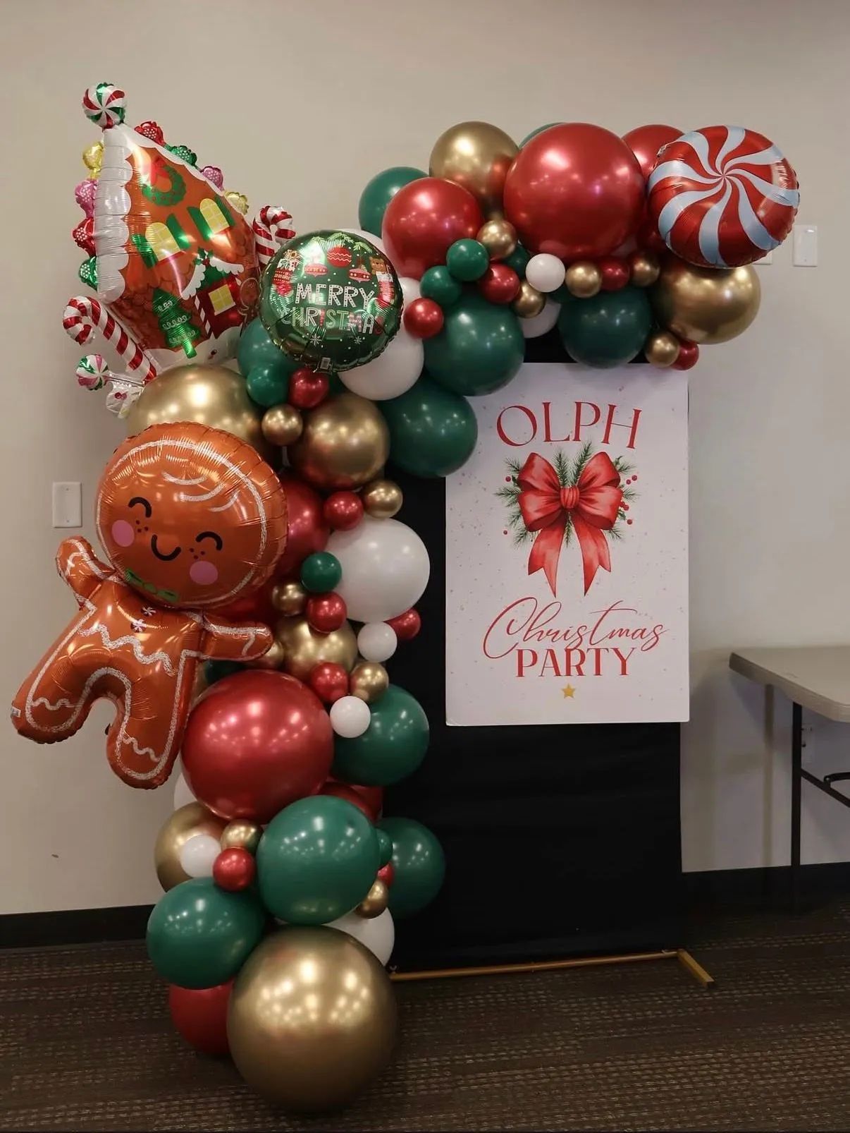 Holiday balloon arch with gingerbread and candy cane decorations beside an “Olde Christmas Party” sign